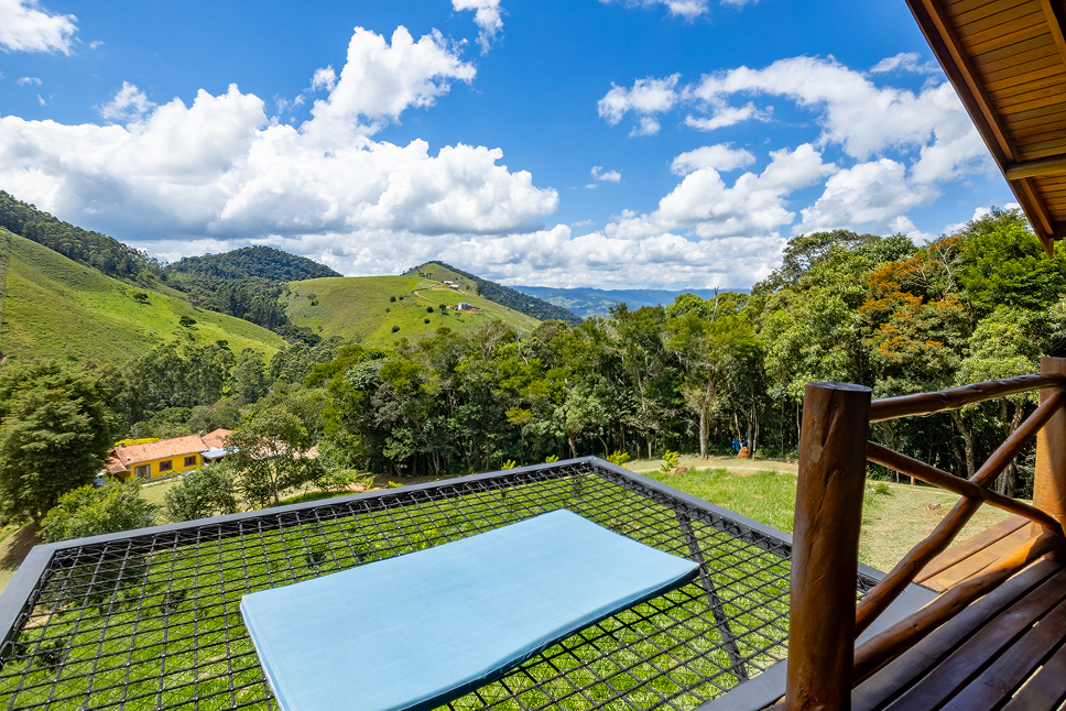 Wooden swing bench with pergola on a wooden deck next to a brick house with a tiled roof under a blue sky.